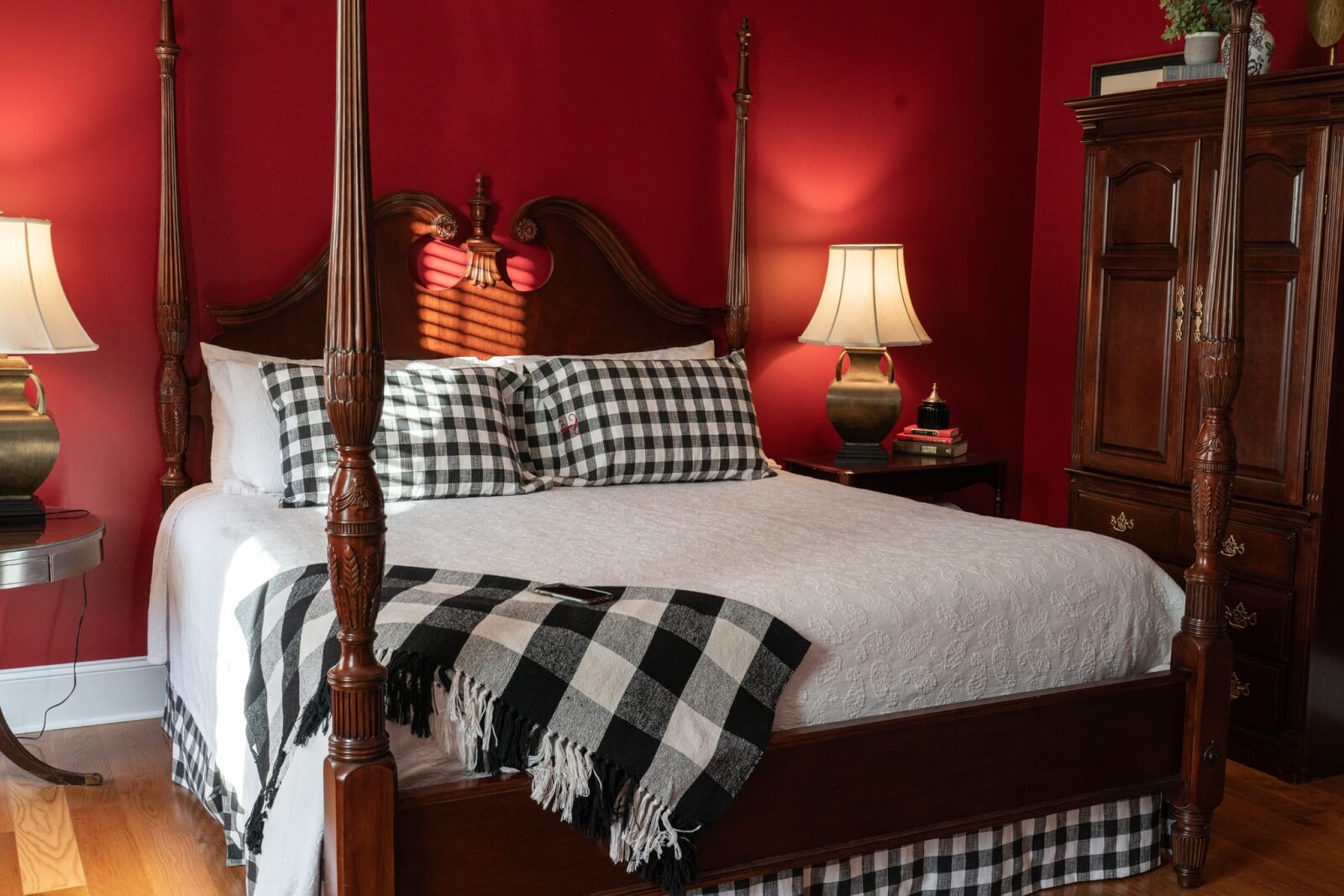 5 Charming Bed & Breakfasts in SC's Old 96 District - 5 A four-poster bed with white bedding and black checkered accents sits in a bedroom with red walls, wooden furniture, and two bedside lamps—perfect for a cozy stay at one of the charming Old 96 District Bed & Breakfasts in SC.