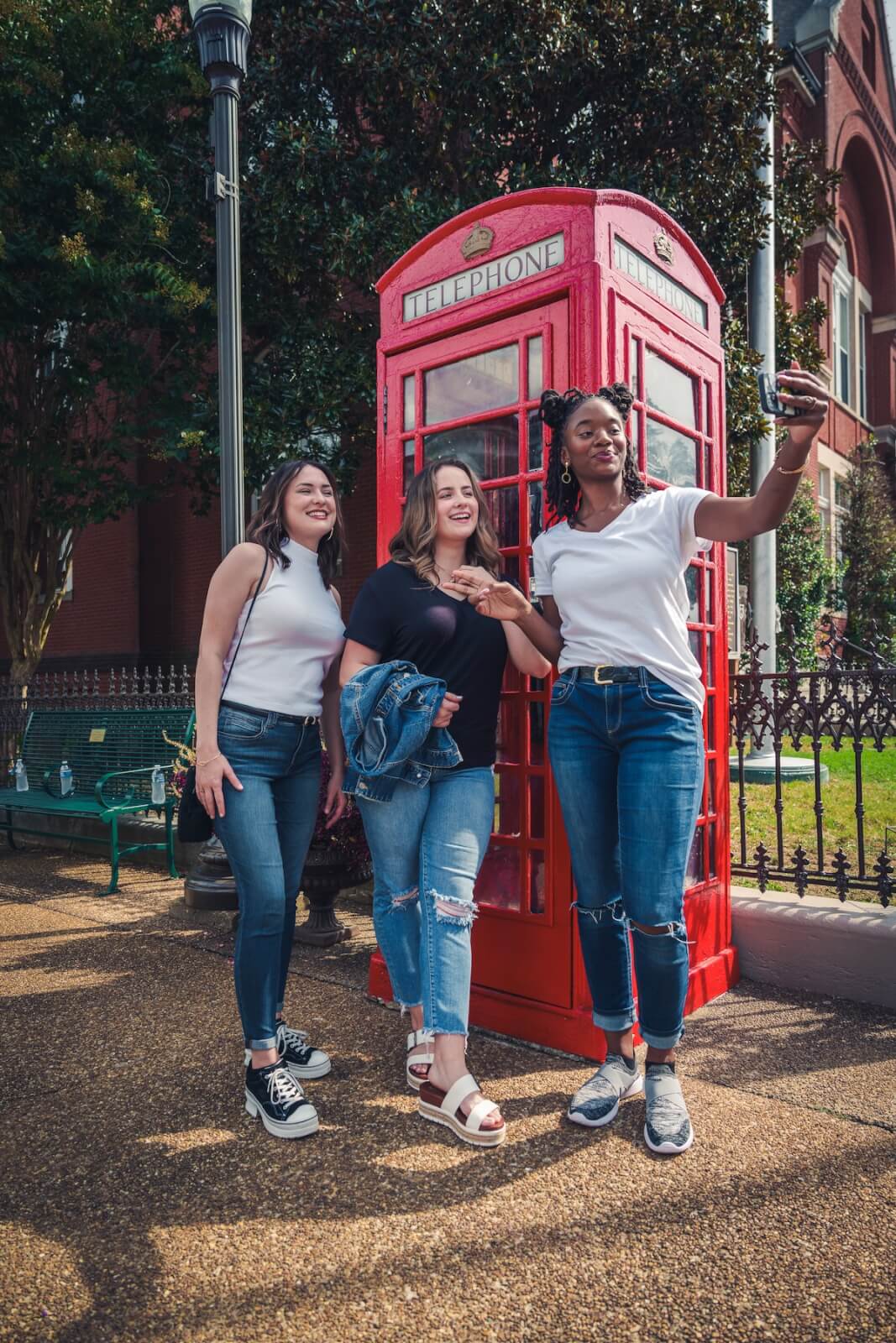 Three women pose for a selfie in front of a classic red British telephone booth on a sunny day, capturing one of the fun Oxford MS things to do on a memorable girls’ weekend.