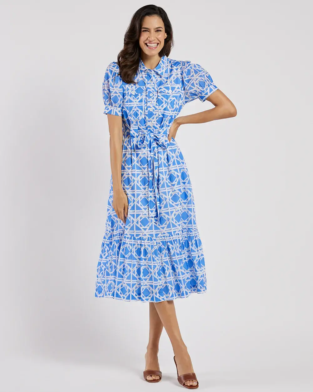 Woman standing and smiling, wearing a blue and white patterned midi dress with short sleeves and brown open-toe heels.