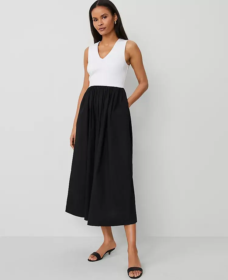 A woman stands against a plain background wearing a sleeveless white top and a high-waisted, ankle-length black skirt with black sandals—an effortlessly chic look.