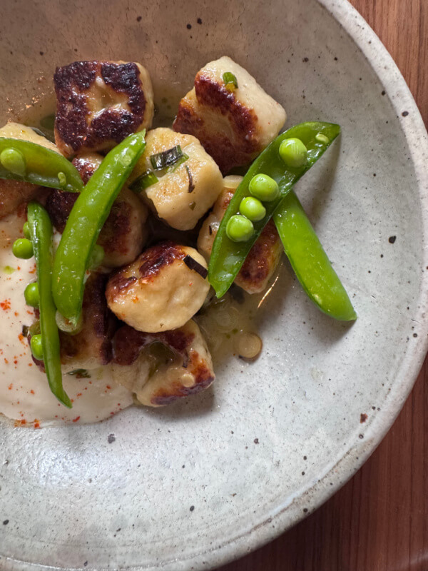 Pan-seared gnocchi with snap peas and creamy white sauce, artfully presented in a ceramic bowl.
