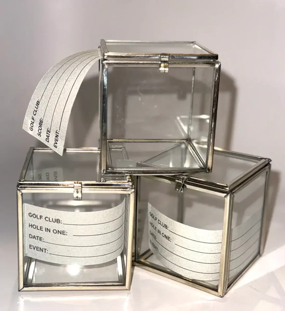 22 Birmingham FINDS for June: Breezy Dresses, Entertaining & Gifts for Dad - 17 Three glass display boxes with metallic edges, each containing a card labeled for golf club, hole in one, date, and event details—perfect for showcasing summer shopping finds or cherished golfing memories.