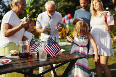 A family gathers outdoors around a wooden table with drinks and American flags.