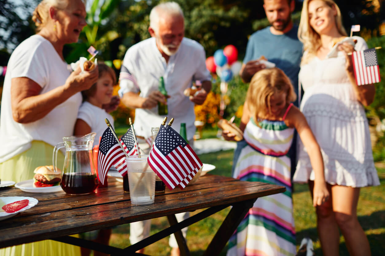 A family gathers outdoors around a wooden table with drinks and American flags, celebrating with food and decorations—capturing the festive spirit often seen at Birmingham events.