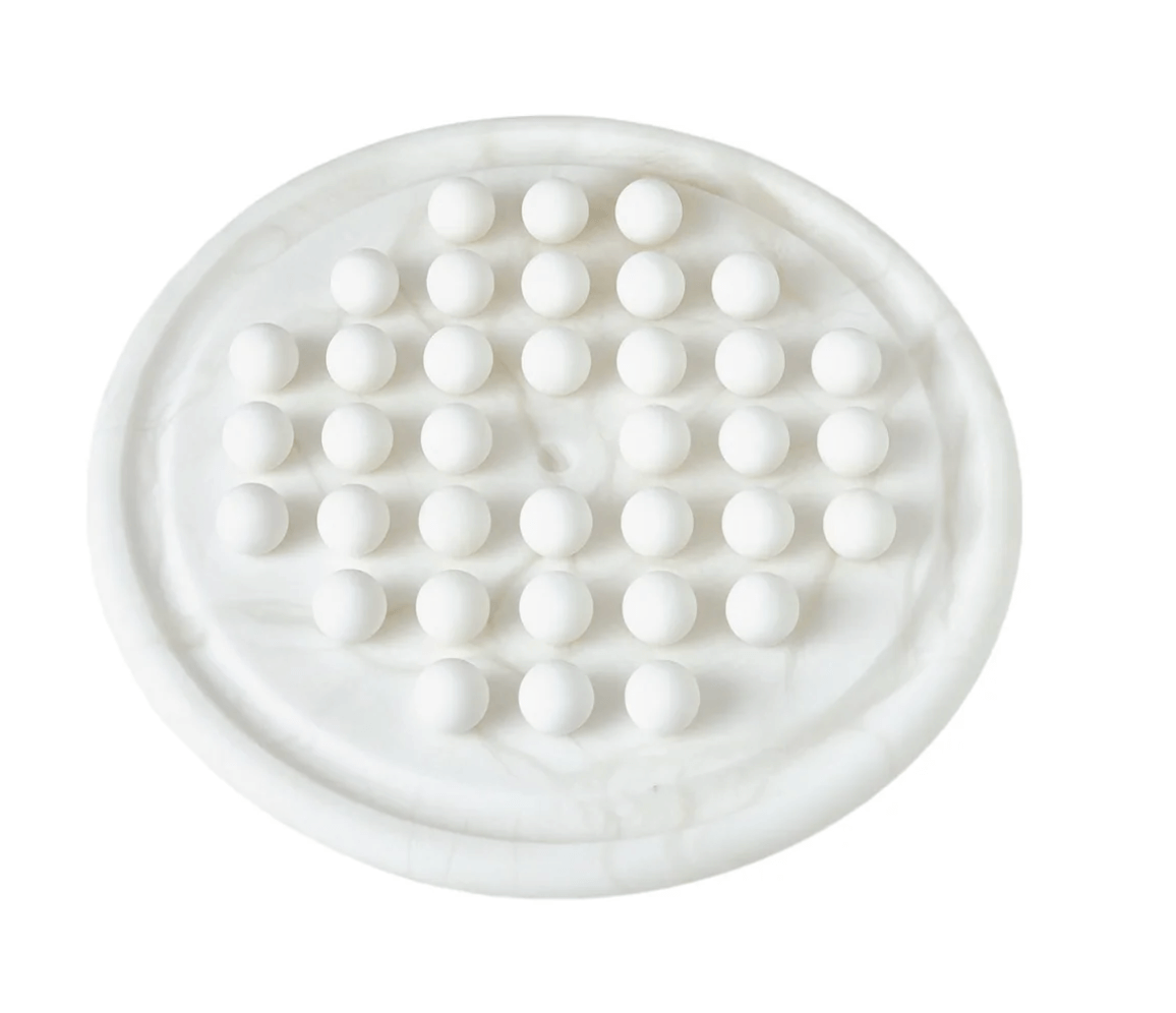 A luxe round white board with a grid of white marbles arranged in rows, resembling a marble solitaire game—a stunning FINDS piece for elegant décor.