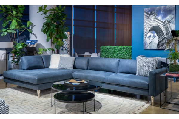 A modern living room with a large blue sectional sofa, two round black coffee tables, decorative pillows, plants, and contemporary wall art—perfect for relaxing during an Independence Day Savings Event.