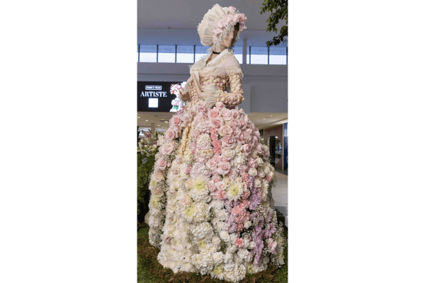 A mannequin dressed in an elaborate gown and bonnet made entirely of pastel-colored flowers stands in a shopping mall as part of the Fleurs de Ville ARTISTE exhibition.