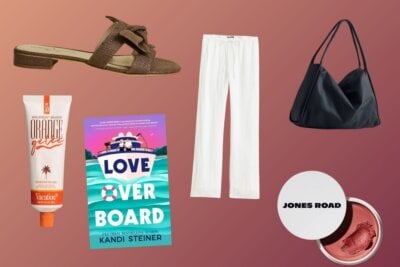 Flat lay of summer essentials: a brown sandal, orange sunscreen, white pants, romance novel, black handbag, and Jones Road makeup set against a gradient pink background.