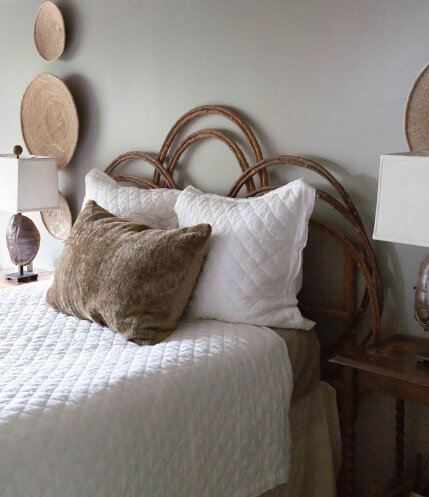 A bed with a white quilted cover and pillows, brown decorative pillow, rattan headboard, two wooden nightstands with lamps, and woven wall decor create a cozy atmosphere inspired by Logos Interiors.
