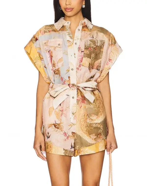 A woman wears a luxurious, short-sleeve, button-up floral romper with two chest pockets, a fabric waist tie, and pastel colors—perfect for July 2025 in Memphis.