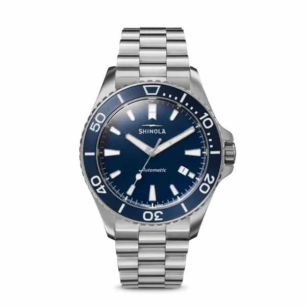 A luxury stainless steel Shinola automatic wristwatch with a blue bezel and dial, silver hour markers, and a metal link bracelet is shown against a black background—perfect for stylish evenings in Memphis come July 2025.