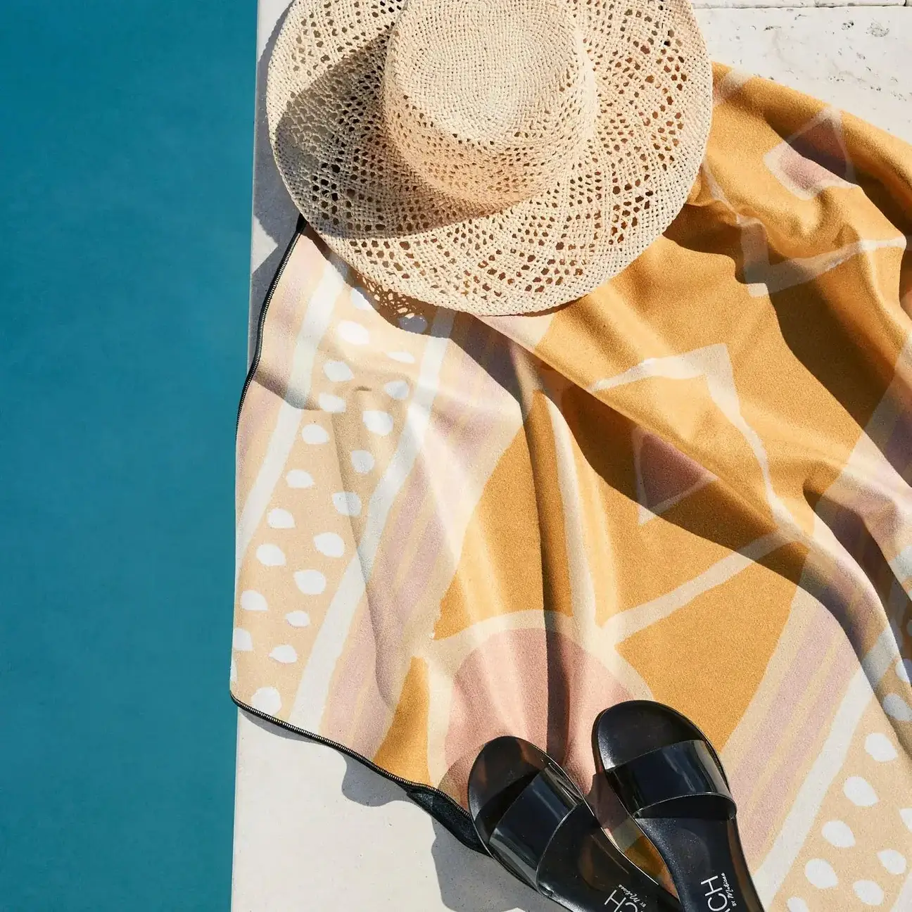 A straw hat, patterned towel, and black sandals—this poolside setup is one of summer 2025’s hot finds, perfect for soaking up the sun next to Memphis's clear blue waters.