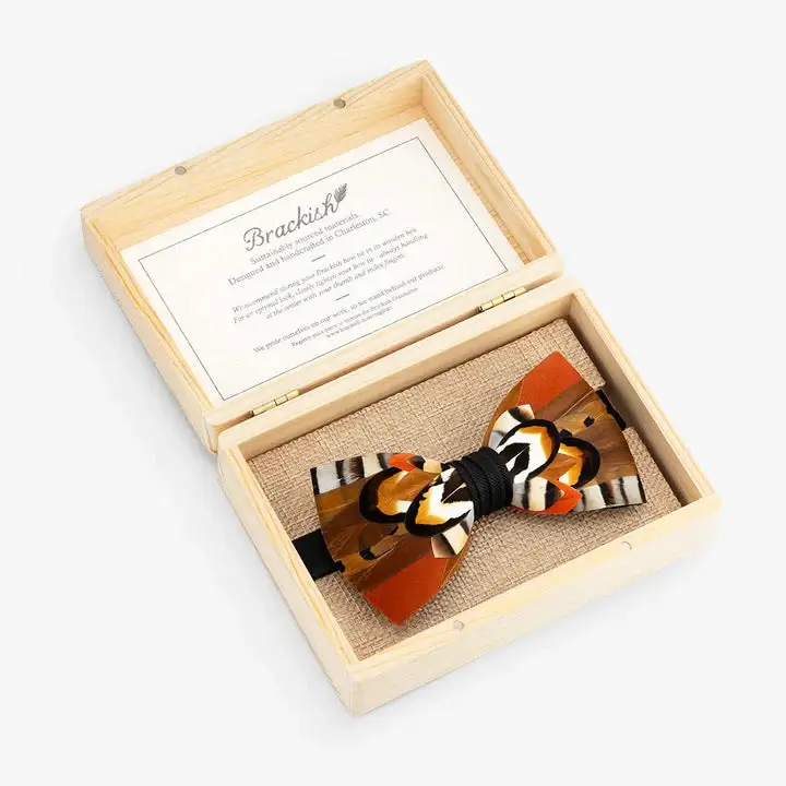A luxurious decorative bow tie with orange, black, white, and yellow patterns is displayed in an open wooden box with a card on the inside of the lid, perfect for making a statement at Memphis events in July 2025.