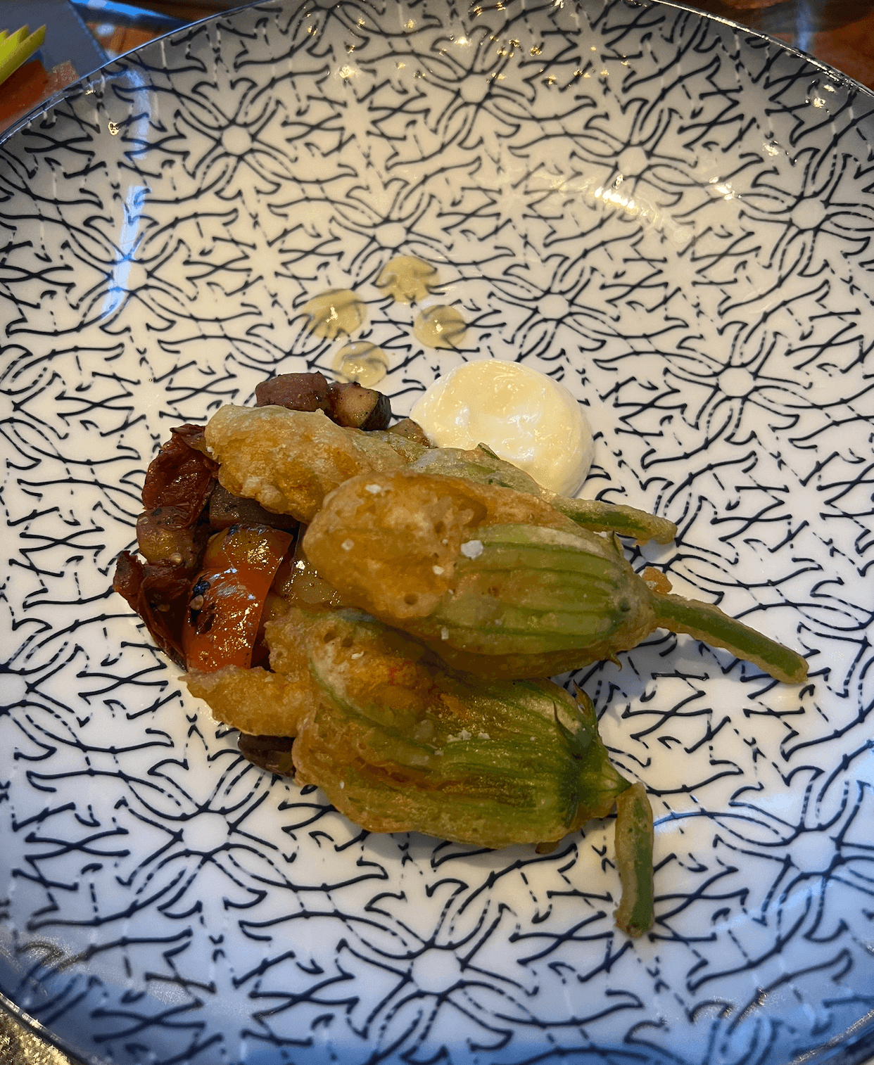 Stuffed zucchini flowers atop roasted vegetables, served with a dollop of white sauce on a patterned black and white plate—a standout dish among Plant-Based Memphis Vegan Eats.
