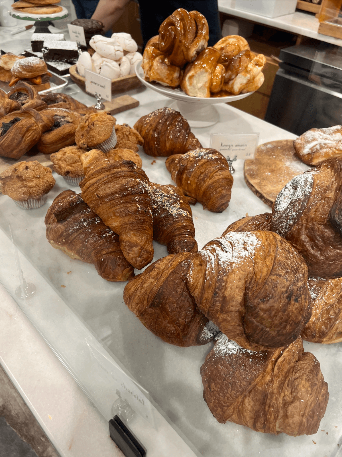 A bakery display case filled with various plant-based pastries, including croissants, muffins, and other baked goods. A person serves treats in the background at this Memphis shop.