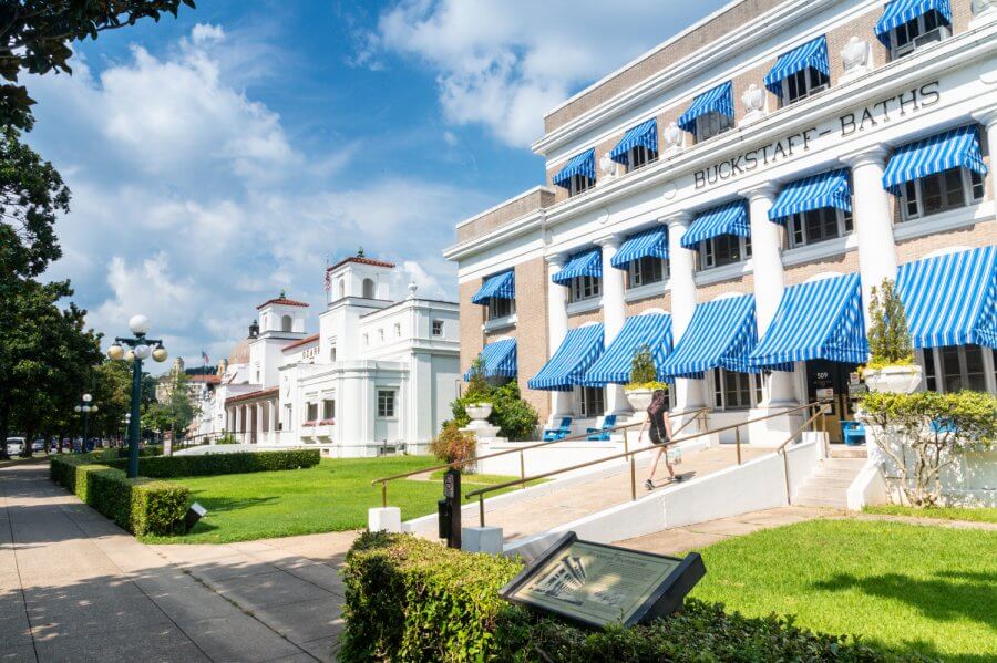Memphis’s 10 Most Popular Articles of 2025 - 11 A person walks past Buckstaff Baths, a historic building with blue-and-white striped awnings, on a sunny day in Hot Springs, Arkansas—a charming spot for weekend getaways from Memphis.