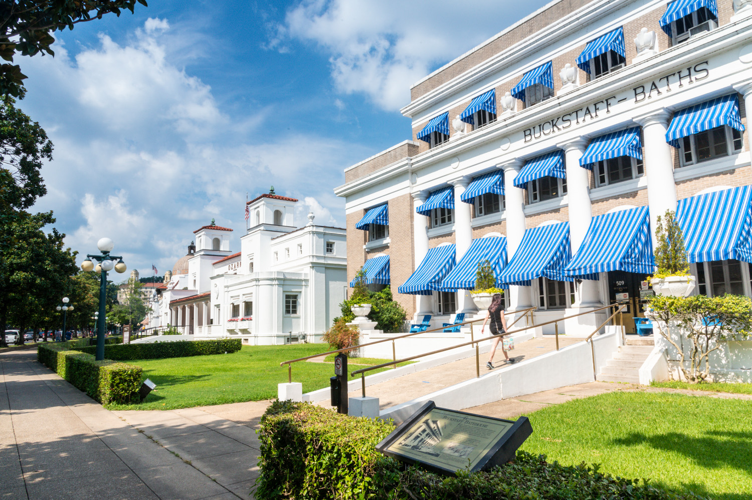 A person walks past Buckstaff Baths, a historic building with blue-and-white striped awnings, on a sunny day in Hot Springs, Arkansas—a charming spot for weekend getaways from Memphis.