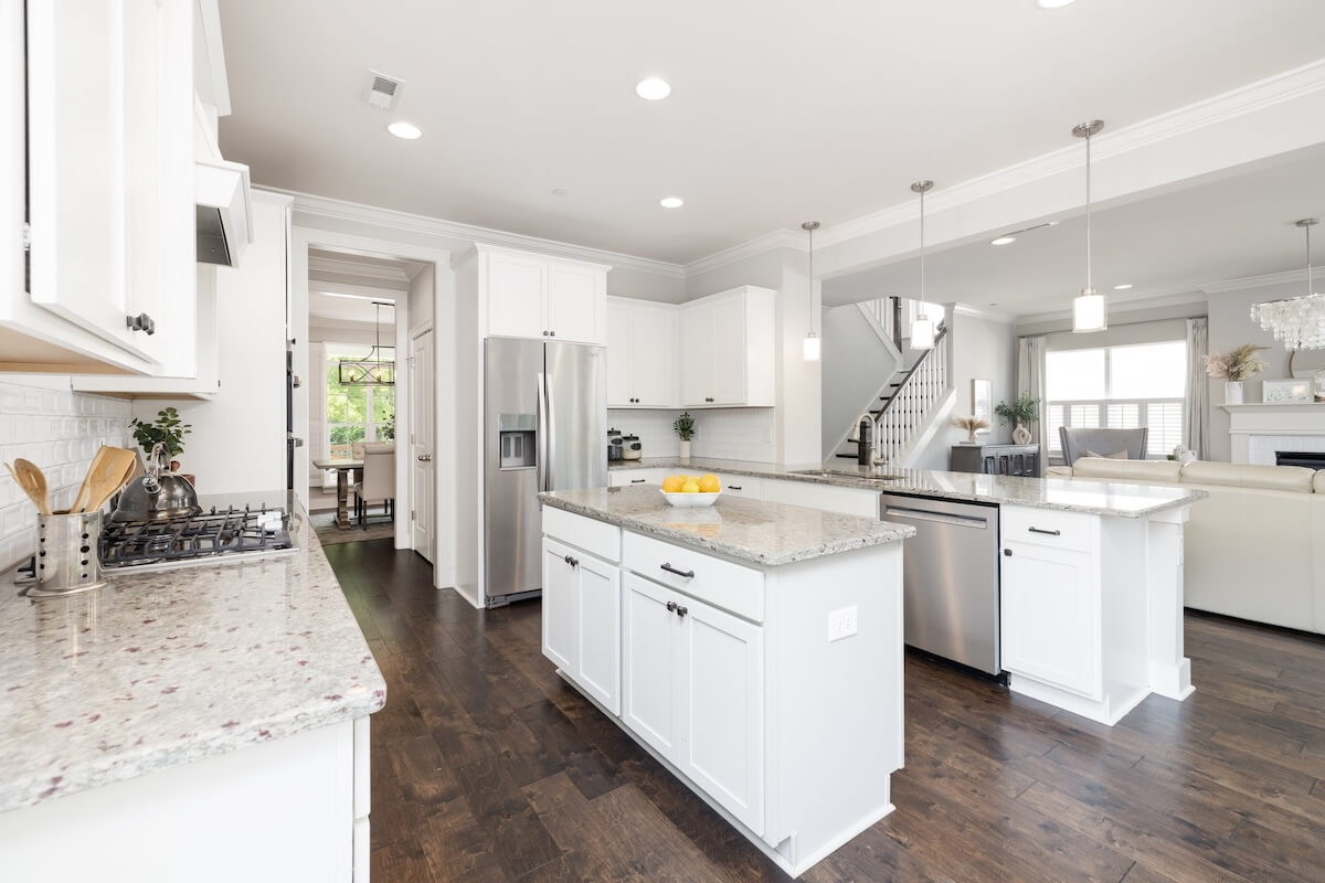 Modern kitchen with white cabinets, granite countertops, and stainless steel appliances centers this Franklin Cottage, open to a living area with hardwood floors and pendant lighting.