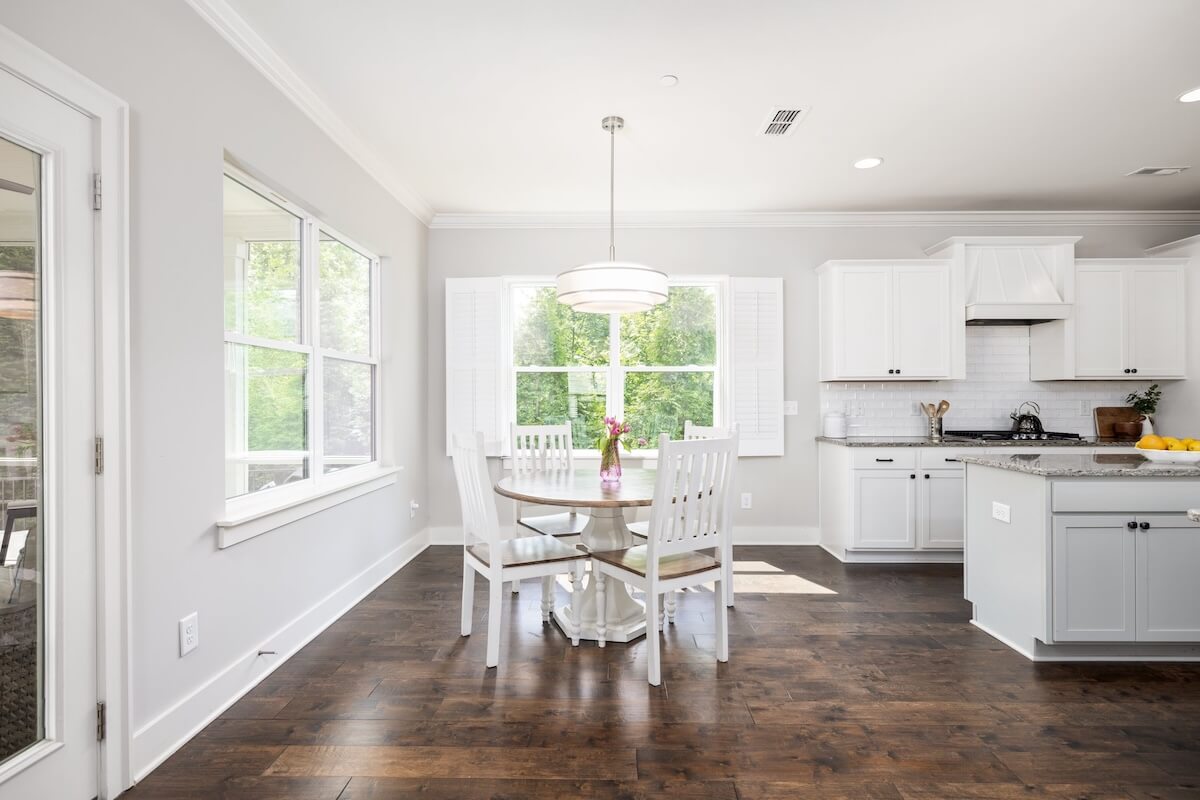 Just Listed! This bright, modern kitchen and dining area at Franklin Cottage features white cabinets, a round table for four, hardwood floors, and large windows that fill the space with natural light.