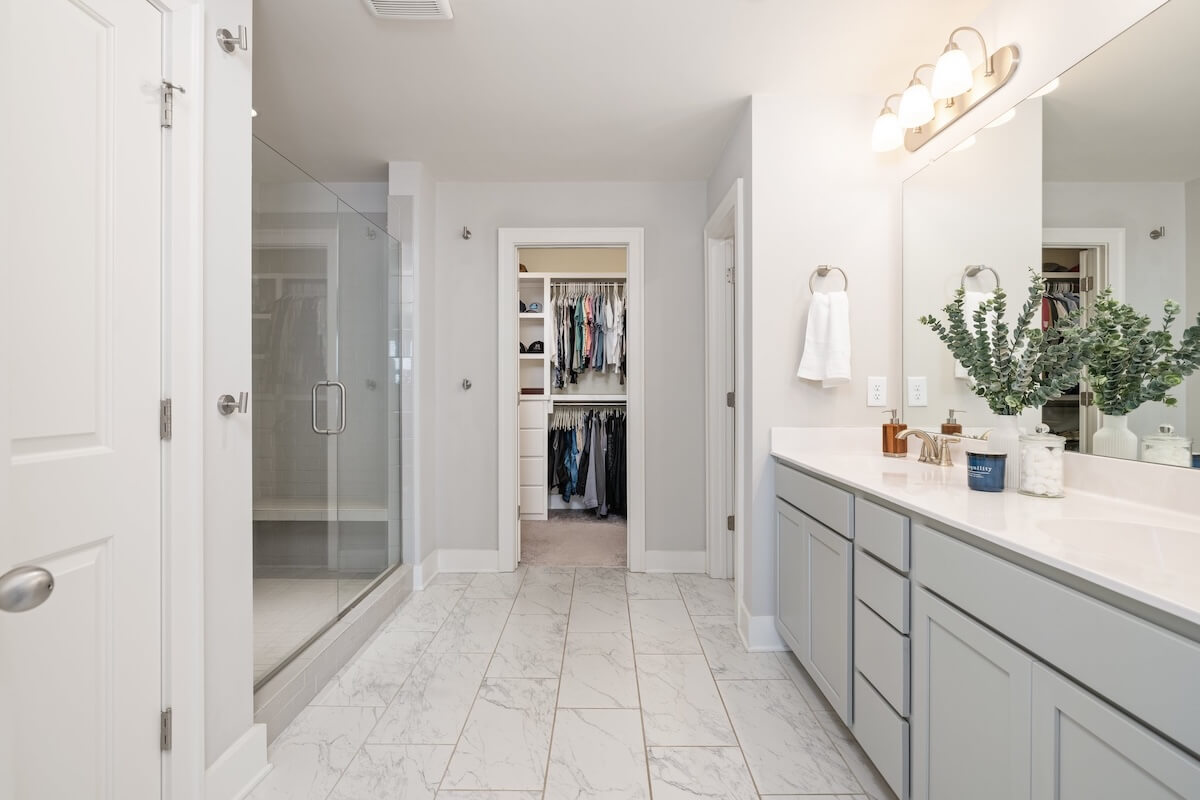 Modern bathroom in this Franklin cottage features light gray cabinets, double sink vanity, large mirror, glass-enclosed shower, and a walk-in closet with organized clothes—just listed and ready to be your own storybook home.