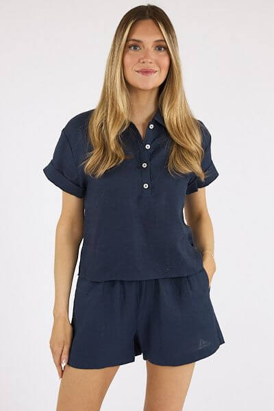 20 Nashville FINDS for June: Father's Day Gifts, Chic Accessories & More - 4 A woman with long, straight hair wears a navy blue short-sleeve button-up top and matching shorts, perfect for shopping Nashville boutiques, as she stands against a plain white background.