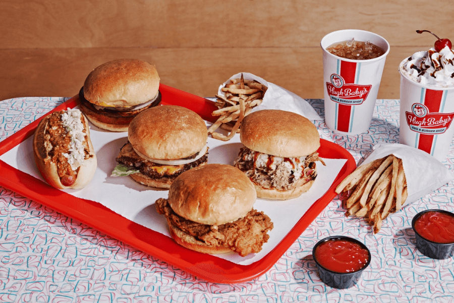 A red tray with four burgers, a chili cheese hot dog, two servings of fries, two cups of soda, and a topped milkshake celebrates Nashville Openings this 4th of July—plus two ketchup containers on the table.