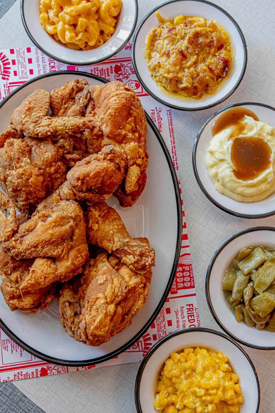 A plate of fried chicken is surrounded by bowls of macaroni and cheese, mashed potatoes with gravy, green beans, creamed corn, and a cheesy casserole—comfort food you'd crave after a night at Nashville music venues.