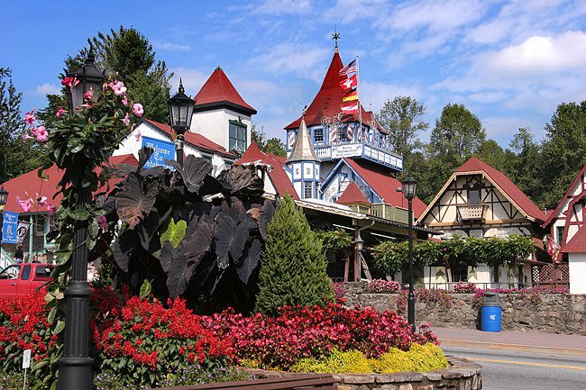 A street scene in a small town with Bavarian-style buildings, red roofs, colorful flowers, and flags under a clear sky—perfect for summer weekend trips from Nashville.