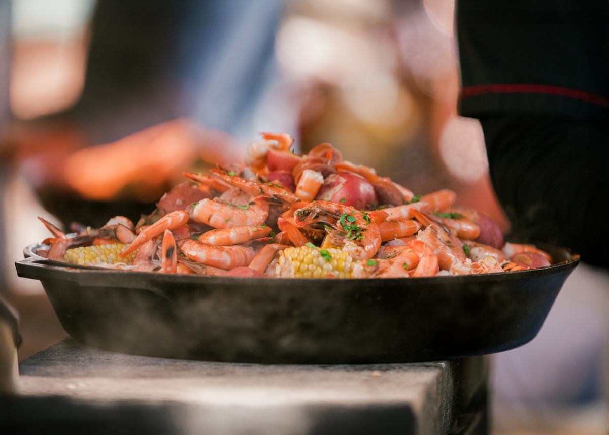A close-up of a pan filled with cooked shrimp, corn on the cob, and seasoning, with steam rising from the food.