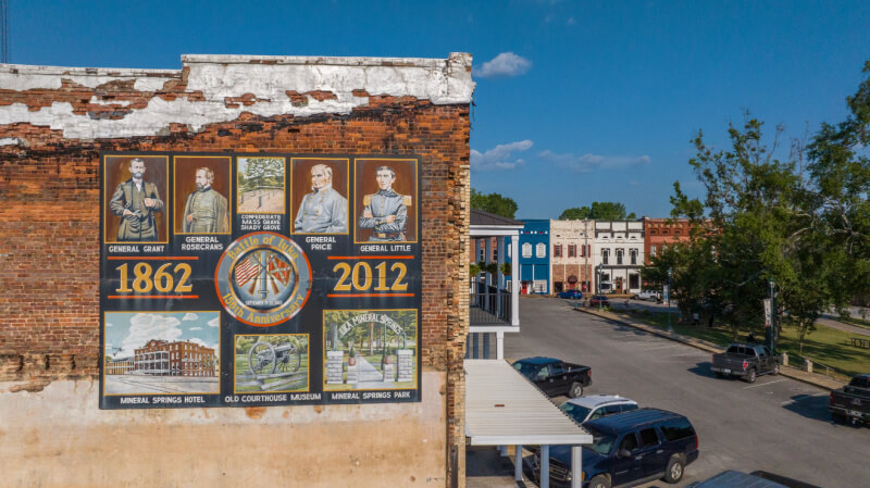A mural on a brick building in Nashville features Civil War generals and historic sites, with the years 1862 and 2012. Shops and parked cars line the street—a perfect stop for summer weekend trips.