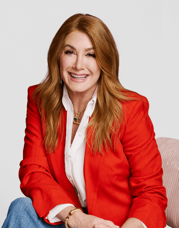 A woman with long auburn hair, inspired by PhD feminine health expert Deeannah Seymour, wears a red blazer over a white blouse and smiles at the camera against a plain background.