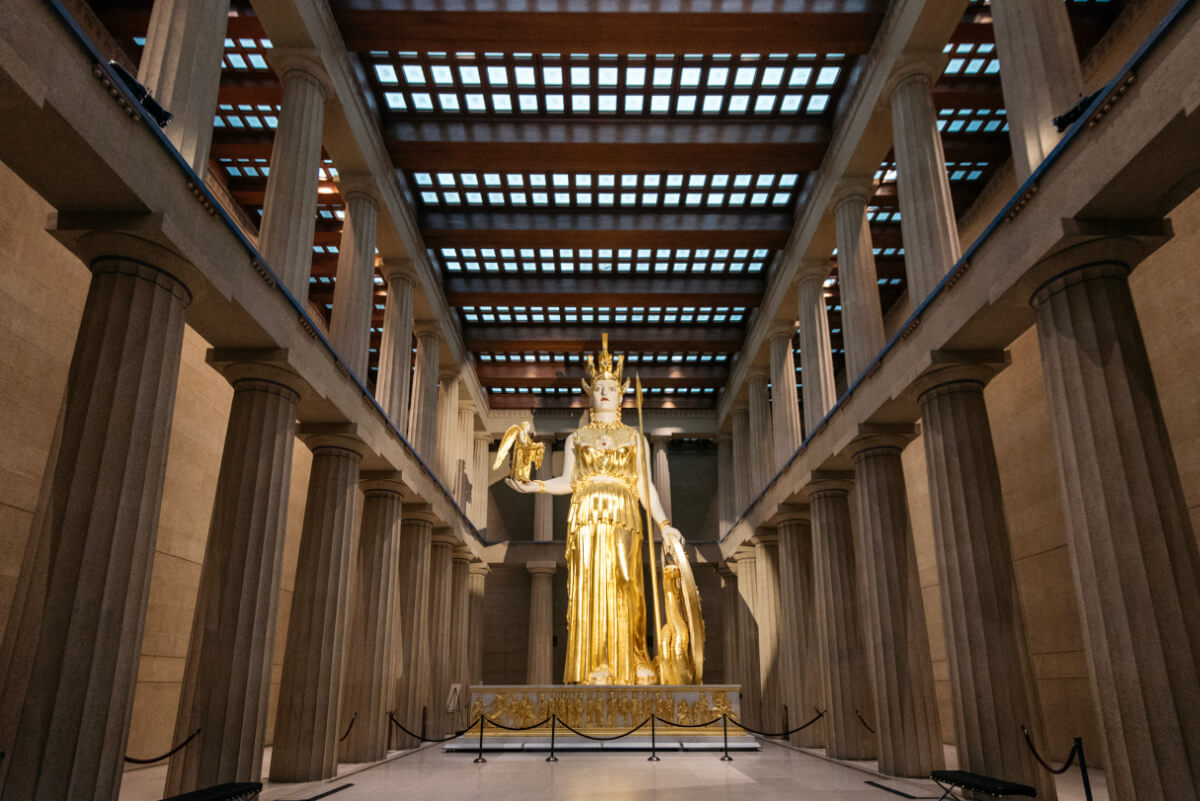Meet Nashville's Own Golden Goddess: Athena Parthenos - 3 A large golden statue of Athena stands in the center of Nashville’s Parthenon, surrounded by tall columns and a high, skylit ceiling.