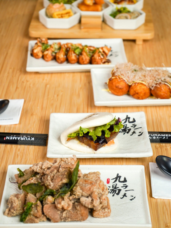 A table with assorted Japanese dishes—including bao buns, takoyaki, meat, and various small appetizers on white plates—captures the vibrant flavors featured at new Nashville restaurants.
