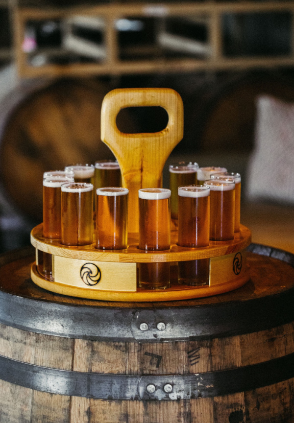 9 New Nashville Restaurants to Try This Month - 4 A wooden carrier holding 12 small glasses of beer is placed on top of a barrel in a rustic setting, perfect for sampling brews at Nashville restaurants or discovering new restaurants opening in June 2025.