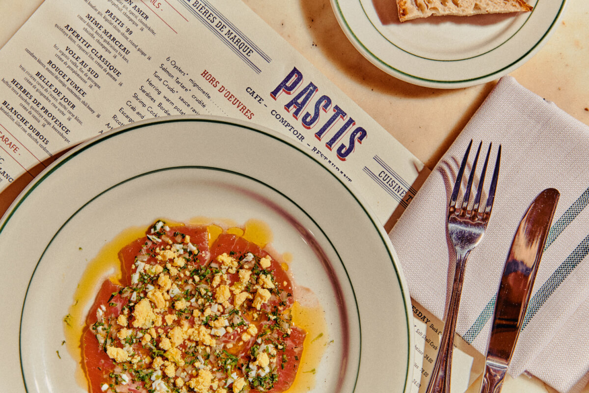 9 New Nashville Restaurants to Try This Month - 5 A plate of crudo with chopped egg and herbs sits on a table next to a menu, bread, and silverware—perfect for sampling the fresh flavors of new restaurants opening in Nashville.
