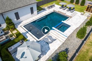 Aerial view of a modern backyard on Cordova Rd, Germantown TN, featuring a rectangular swimming pool, attached hot tub, lounge chairs, and umbrellas on a stone patio.