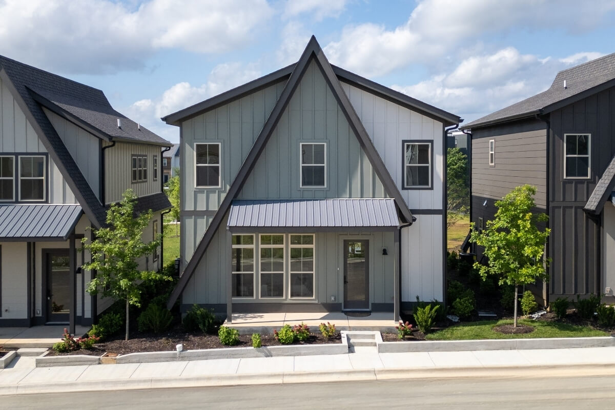 A modern two-story house with a steep A-frame roof, large front windows, and landscaped front yard sits in Nashville’s Morningside Manor neighborhood, basking in the sun on a bright day.