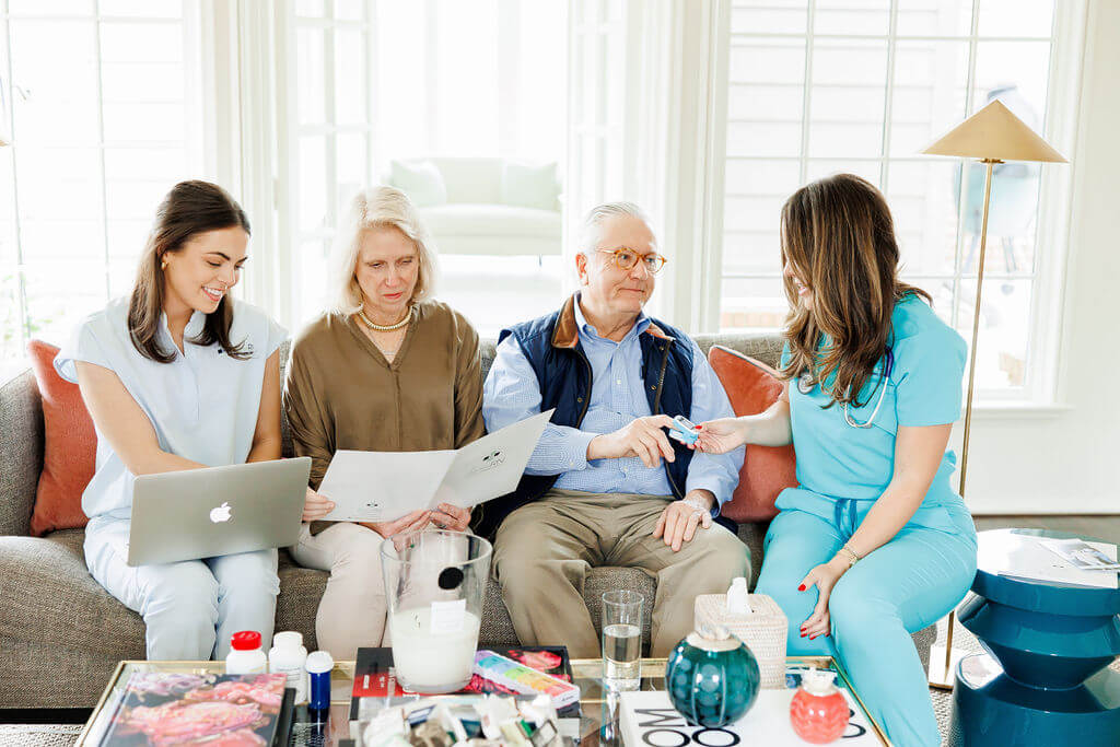 Four people sit on a couch; a nurse from HomeRN Nashville hands medication to an older man, while two women, one with a laptop, review paperwork. Medical supplies are on the table, highlighting the support of home healthcare.
