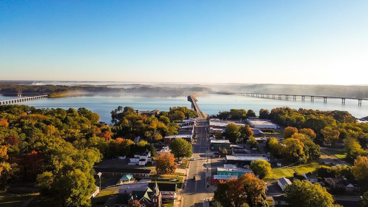 Aerial view of a small town—one of the best towns in Virginia—with a river, two long bridges, and trees showing early autumn colors under a clear blue sky. Perfect for weekend getaways in Virginia.