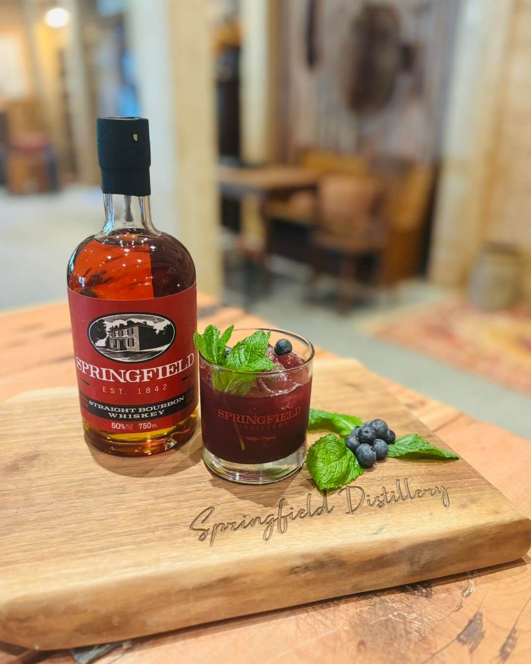 A bottle of Springfield whiskey and a cocktail garnished with mint and blueberries sit on a wooden board engraved with "Springfield Distillery"—a perfect taste of one of the best towns in Virginia.