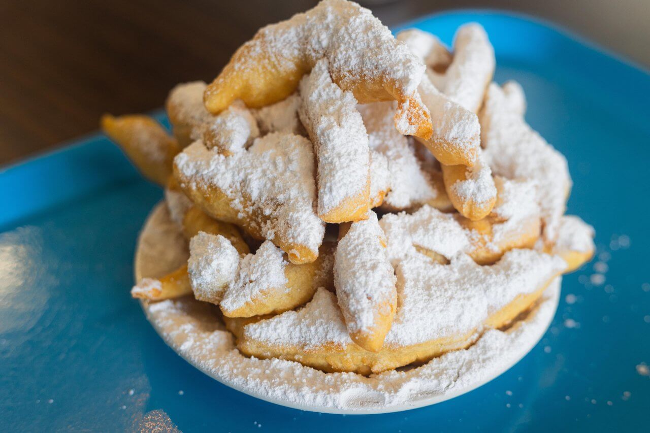 A plate stacked with fried dough pastries generously dusted with powdered sugar, placed on a blue tray—perfect for sharing after a game day stroll through classic SEC Towns.
