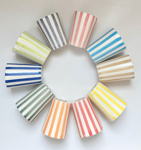 Nine ceramic cups with vibrant Cabana Stripes in various colors are arranged in a circle on a white surface, their openings facing inward.