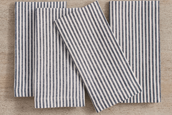 Four blue and white cabana stripes cloth napkins are neatly arranged on a light wooden surface.