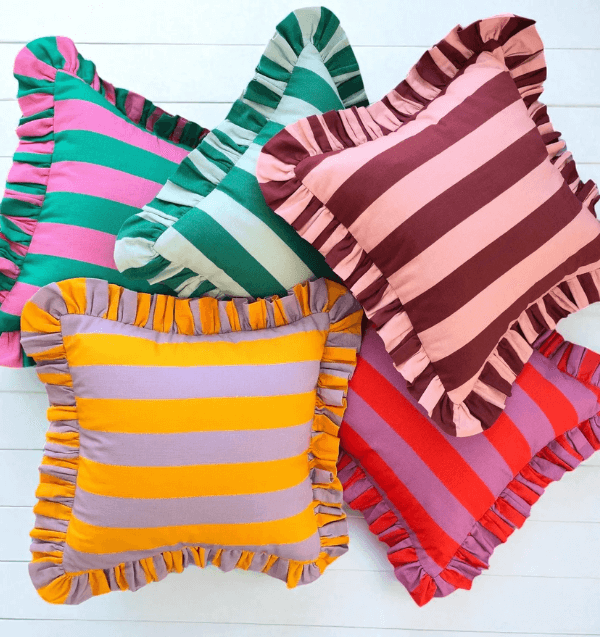 Five square pillows with colorful cabana stripes and ruffled edges, arranged overlapping each other on a white surface.