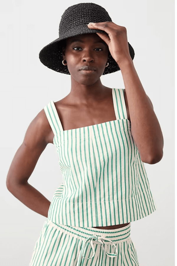 Woman wearing a black sunhat, green-and-white cabana stripes sleeveless top, and matching shorts, standing against a plain background.