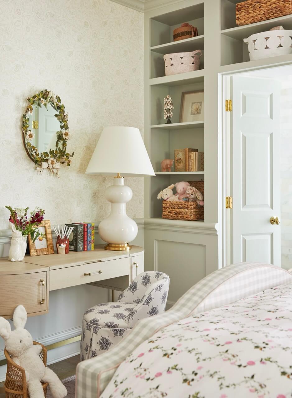 A cozy bedroom in a South Carolina retreat with a floral bedspread, a desk with books and a lamp, shelves with baskets and decor, and a plush bunny on a chair—perfect for soaking in lakeside beauty and historic charm.