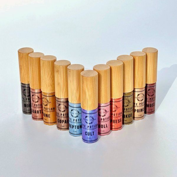 Twelve bottles of Potion Polish nail polish with wooden caps are arranged in a V-shape on a white background for the Memphis FINDS August 2025 collection. Each bottle showcases a unique color and label name.