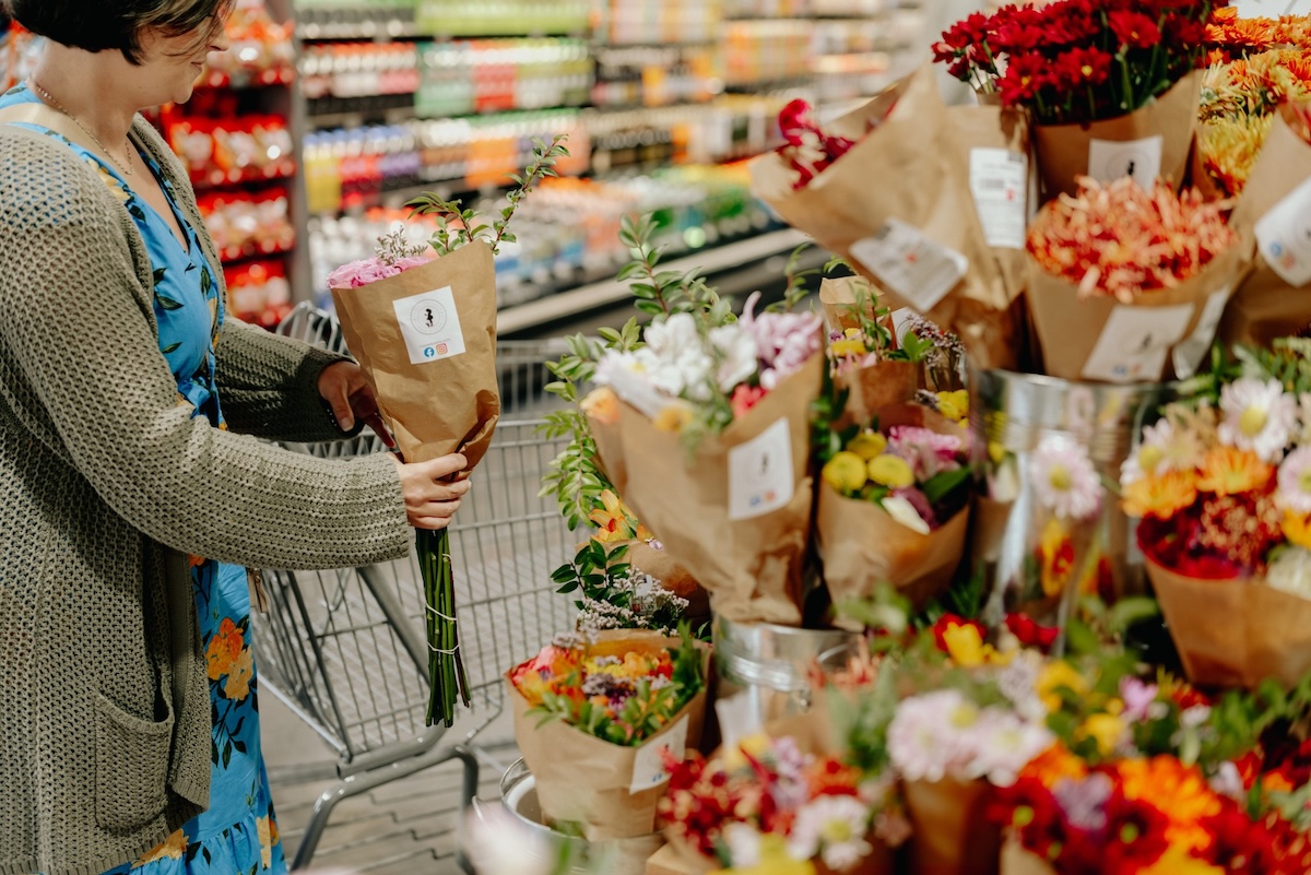 A person in a blue dress selects a bouquet of flowers from a display in a grocery store, reminiscent of the vibrant selections found at boutiques in Memphis.