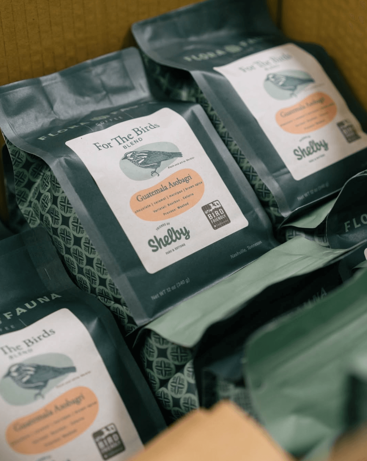 18 Nashville FINDS for Late Summer: Jewelry, Decor & More - 4 Several bags of "For The Birds" Guatemala Asobagi Shelby coffee are stacked in a box at FINDS Nashville, their green packaging and printed labels perfectly capturing the vibrant feel of late summer.