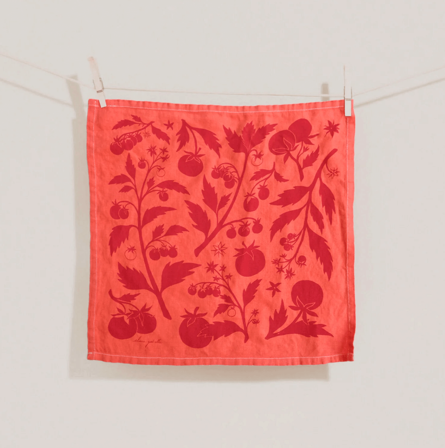 18 Nashville FINDS for Late Summer: Jewelry, Decor & More - 1 A red cloth napkin with a darker red botanical pattern featuring tomatoes and leaves hangs on a clothesline with two clothespins—a charming Late Summer Find inspired by the vibrant spirit of Nashville.